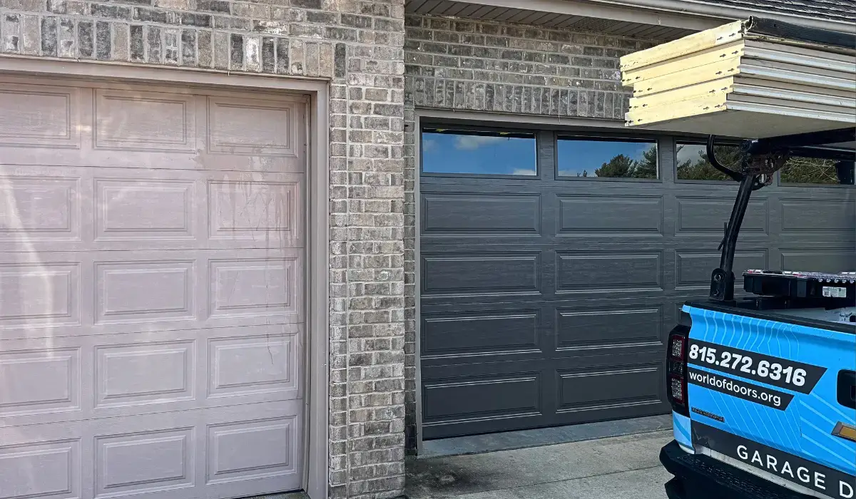 A newly replaced dark gray garage door beside an old, faded door, with a service truck parked nearby.