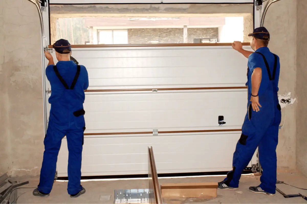 Two technicians installing new white garage door panels inside residential garage during professional panel replacement service.